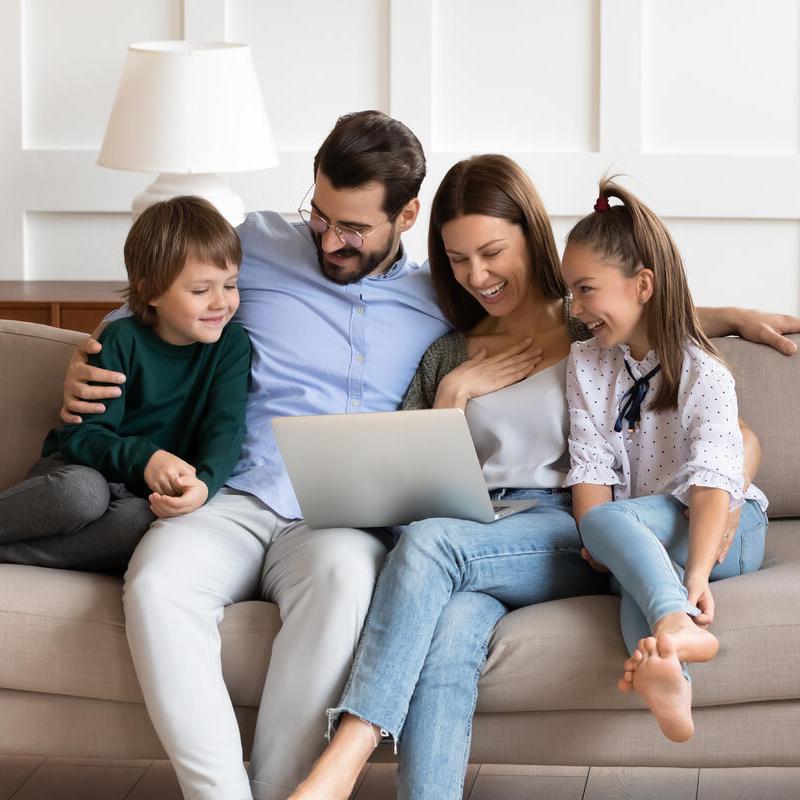 Eine Familie sitzt auf dem Sofa und betrachtet etwas auf dem Laptop